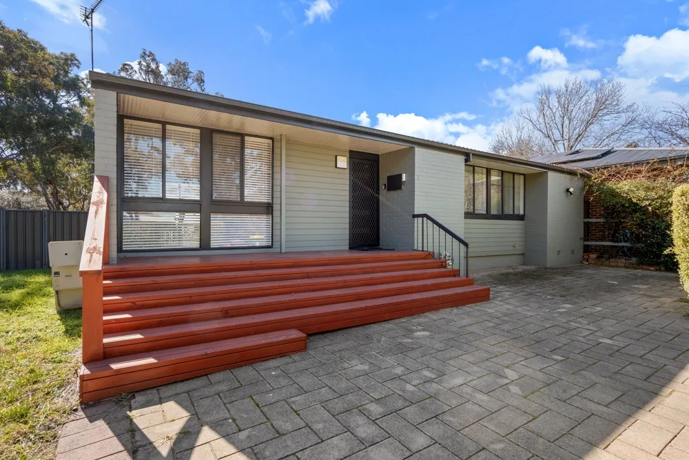 A modern house exterior with a broad wooden deck and paved driveway.