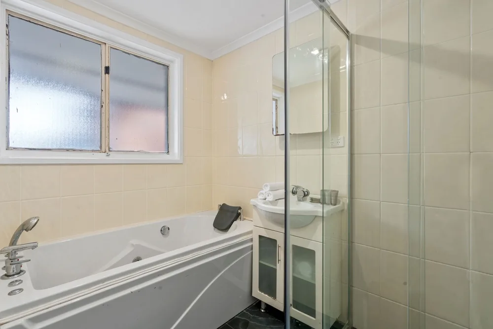 A tiled bathroom with a bathtub, sink, and glass shower screen.