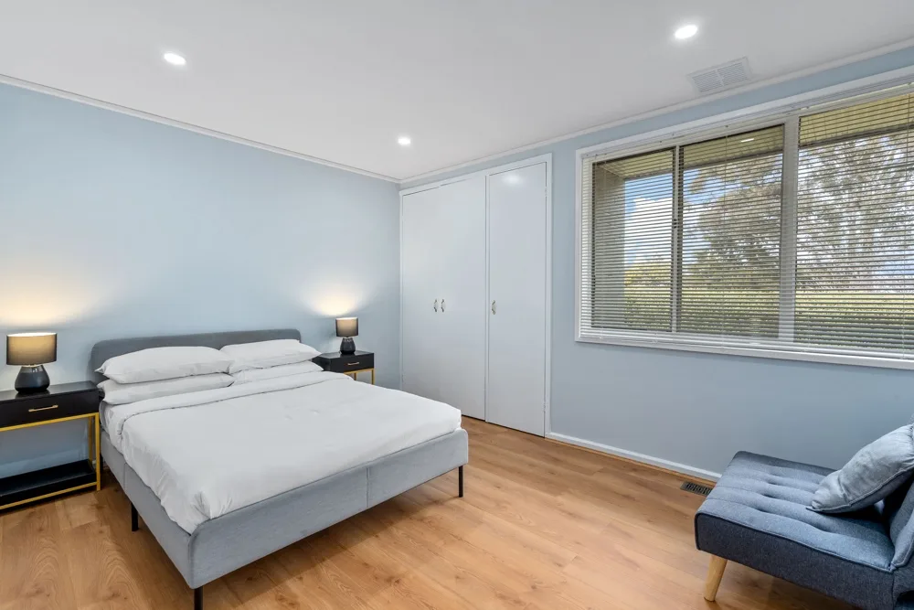A bedroom with a made bed, built-in storage, and a window.