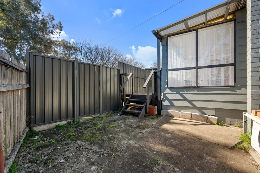 A fenced outdoor patio beside a house, with a small raised wooden platform.