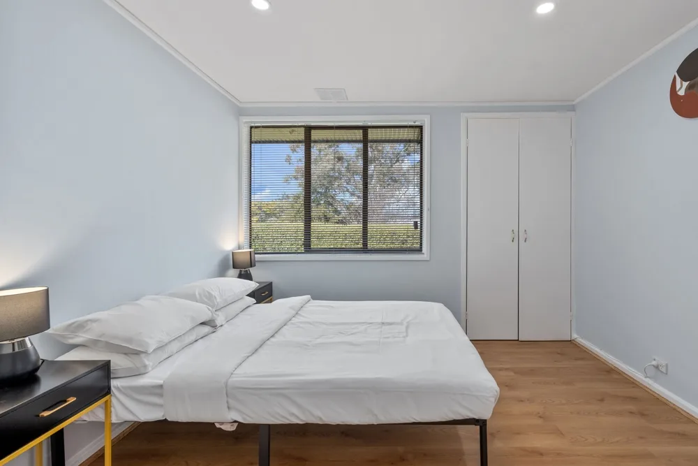 A bedroom with a neatly made bed and a window overlooking greenery.