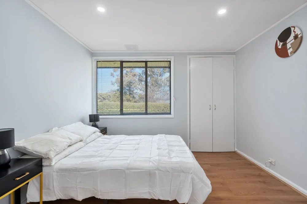 A bright bedroom with a neatly made bed and a window overlooking trees.