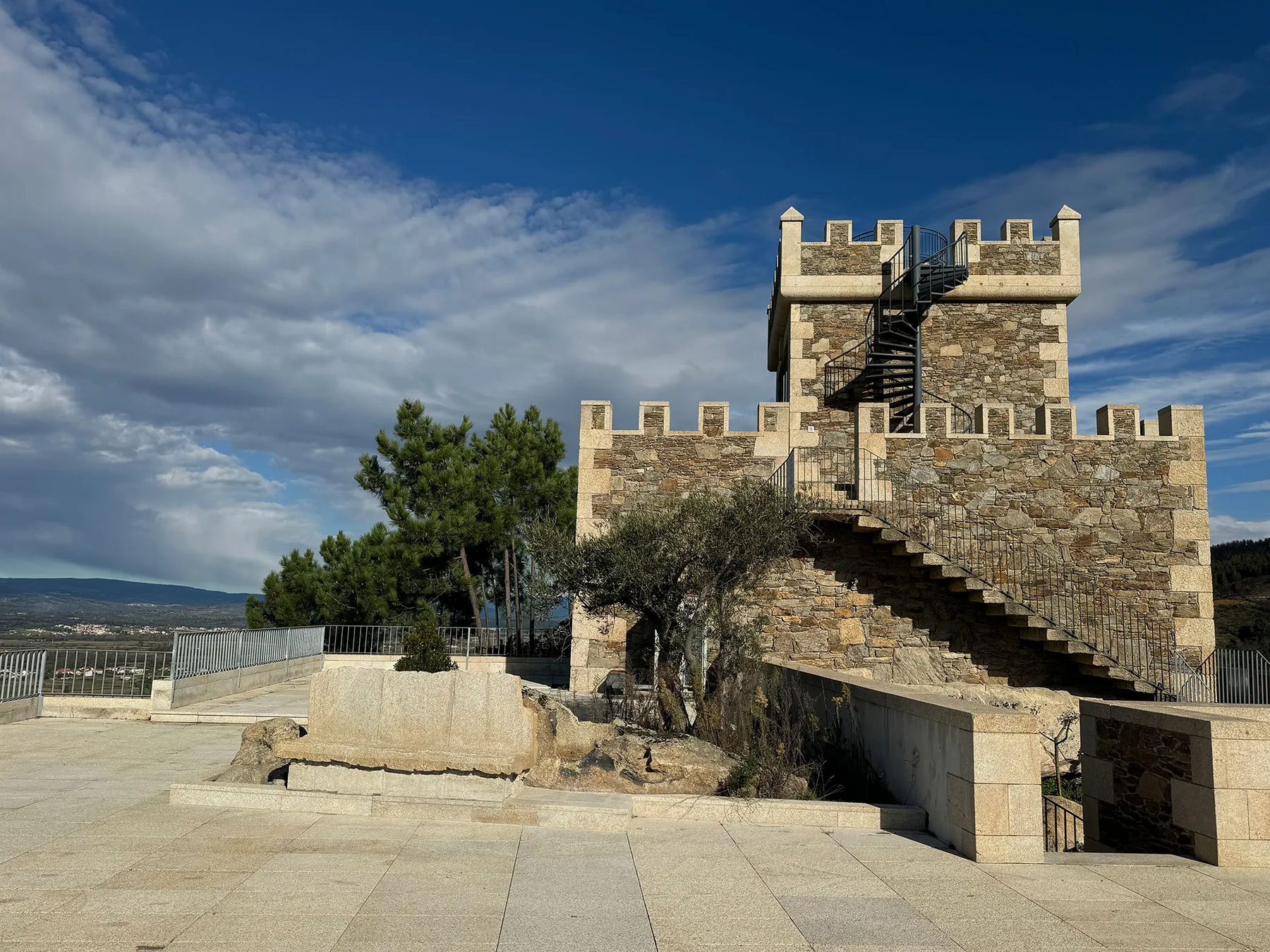 Espacio representativo del hotel: Una torre de piedra con escaleras exteriores se alza junto a un patio pavimentado.