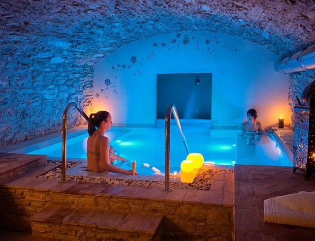 Espacio representativo del hotel: Una piscina interior iluminada en azul bajo un arco de piedra, con personas en el agua.
