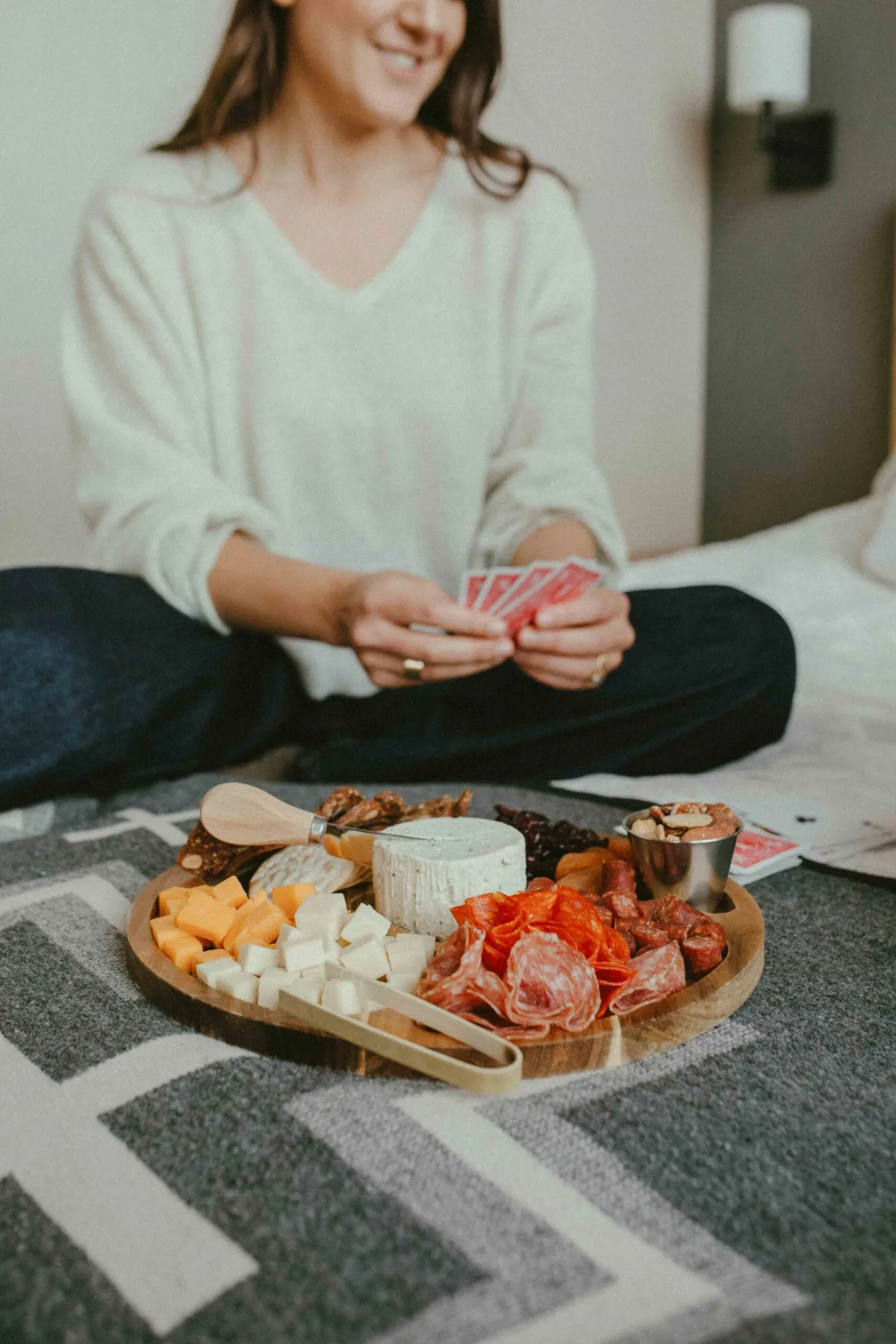 Representative hotel space: A person sits on a bed holding cards beside a platter of assorted snacks.