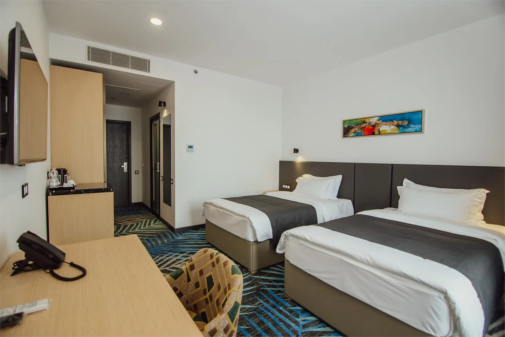 Espacio representativo del hotel: Habitación de hotel con camas, un escritorio y una alfombra estampada.