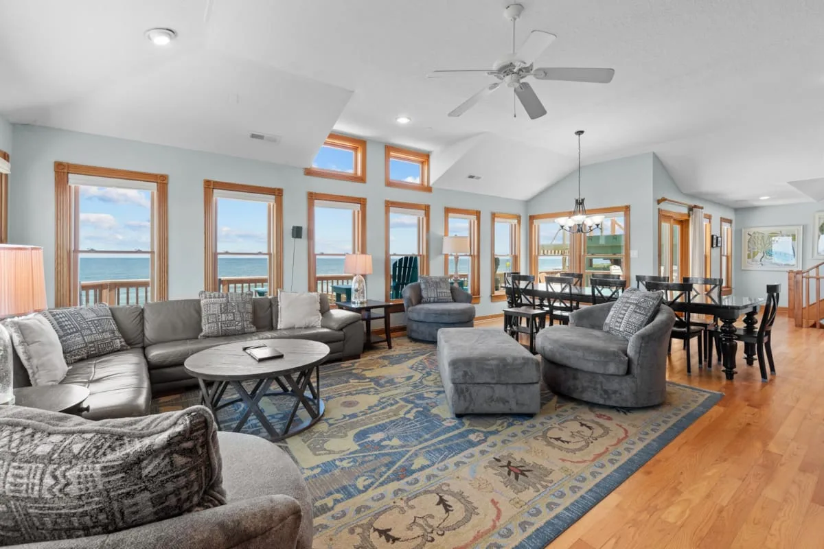 A bright living and dining area with seating, large windows, and a patterned rug.