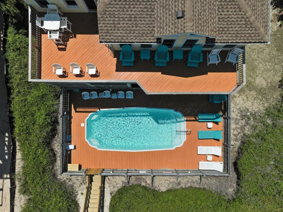 An aerial view shows a swimming pool and surrounding wooden deck beside a building.
