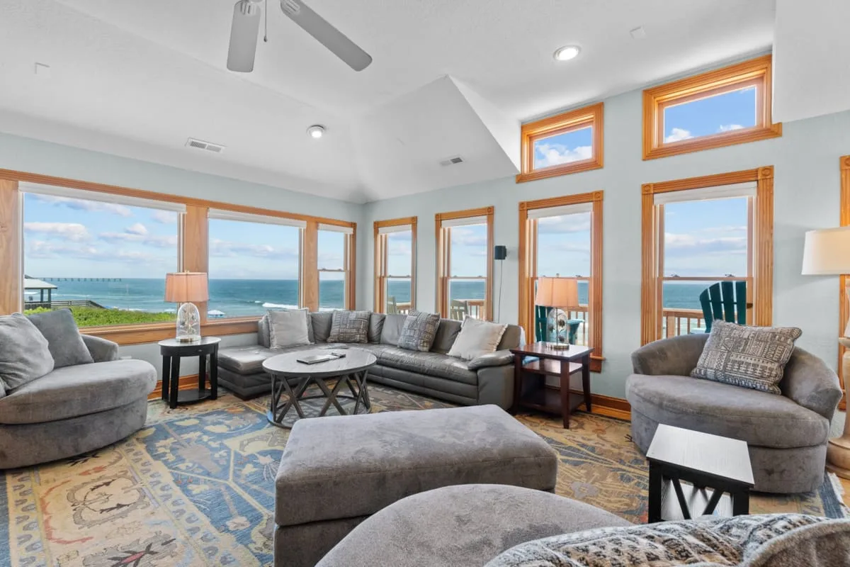 A spacious living room with seating arranged around a coffee table and ocean views through large windows.