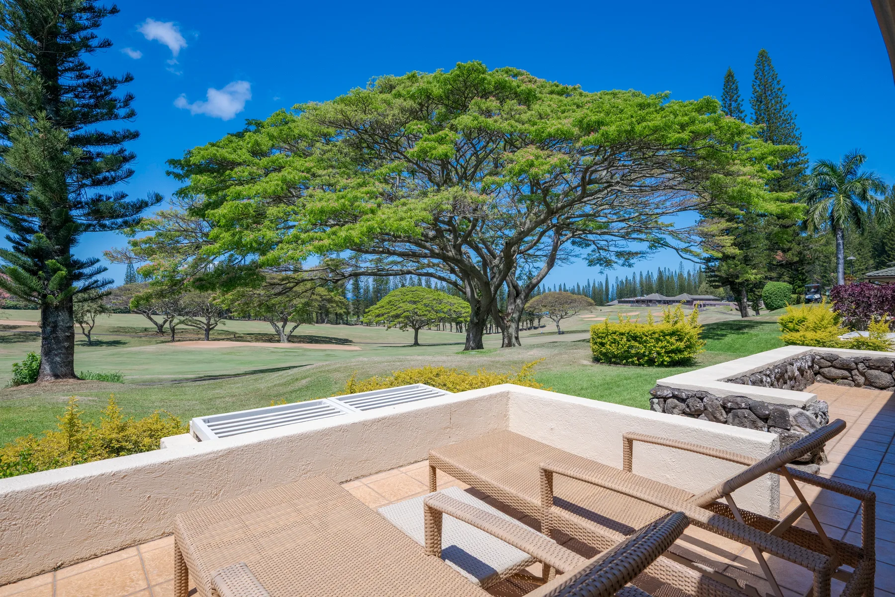 An outdoor patio with seating overlooks a broad green lawn and large trees.