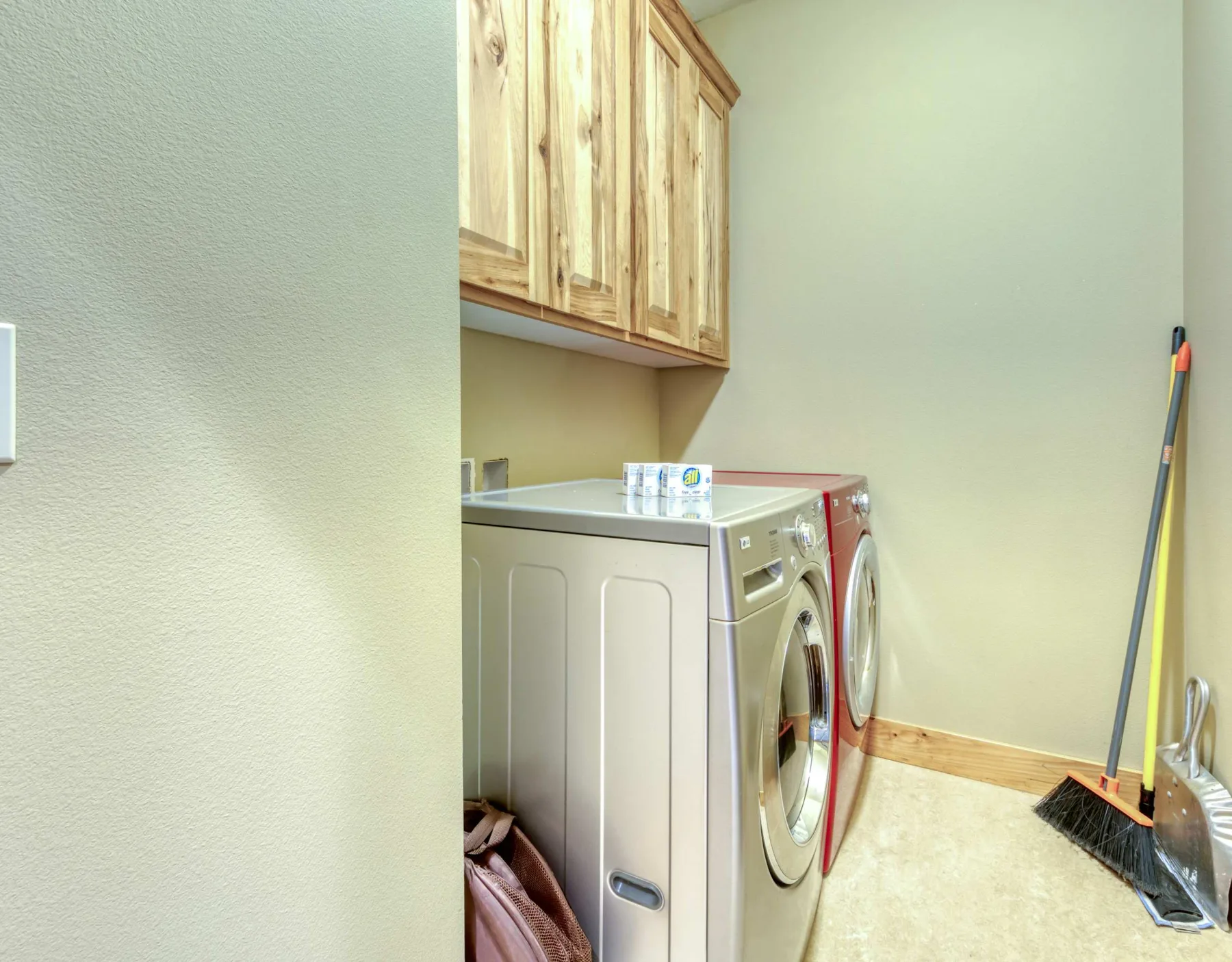 A laundry room with a washer and dryer beneath wooden cabinets.