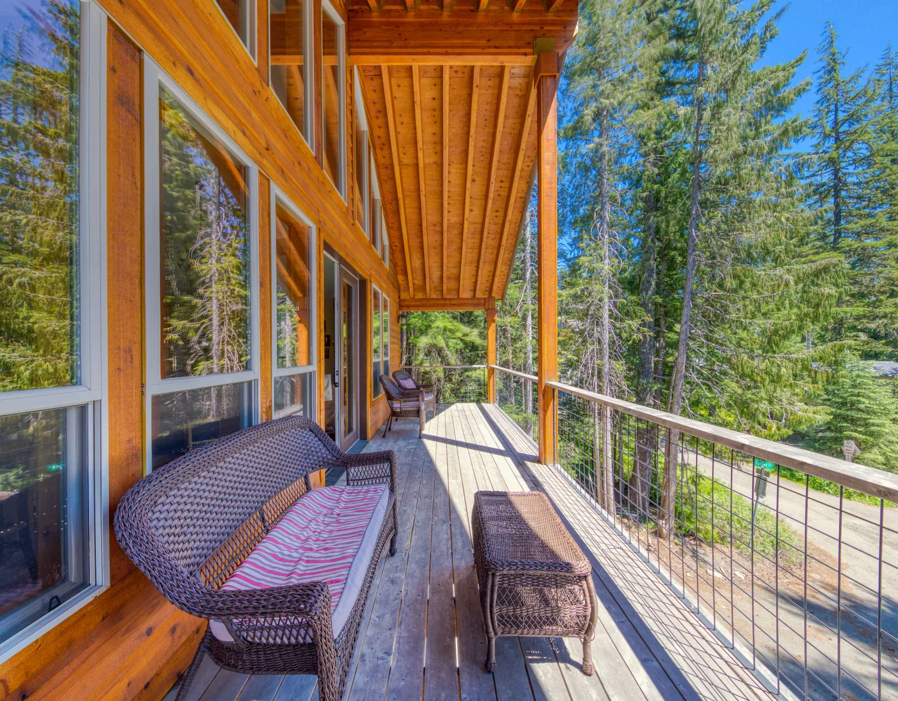 A covered wooden deck with outdoor seating overlooks a forest.