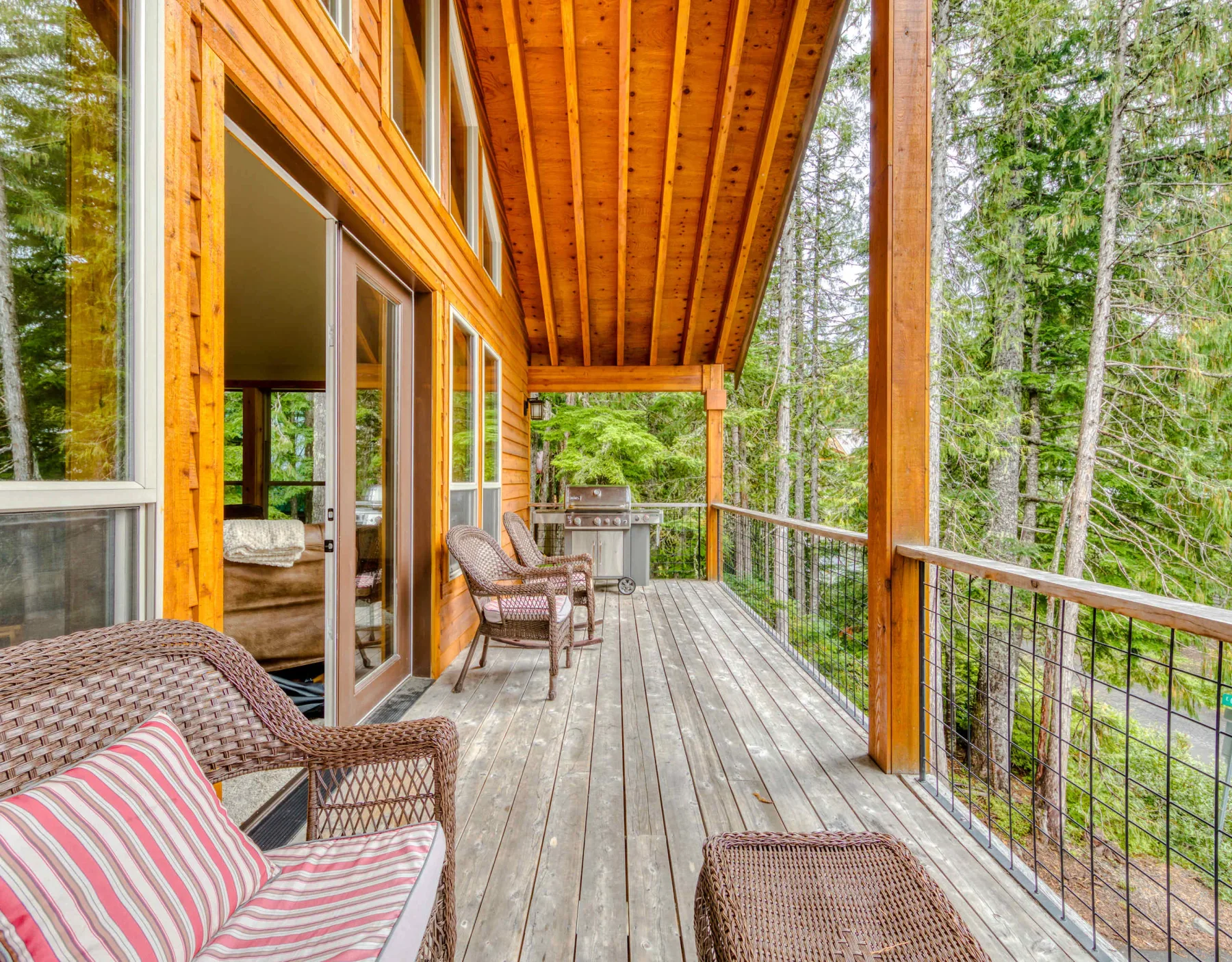 A covered wooden deck with outdoor seating overlooks a wooded area.