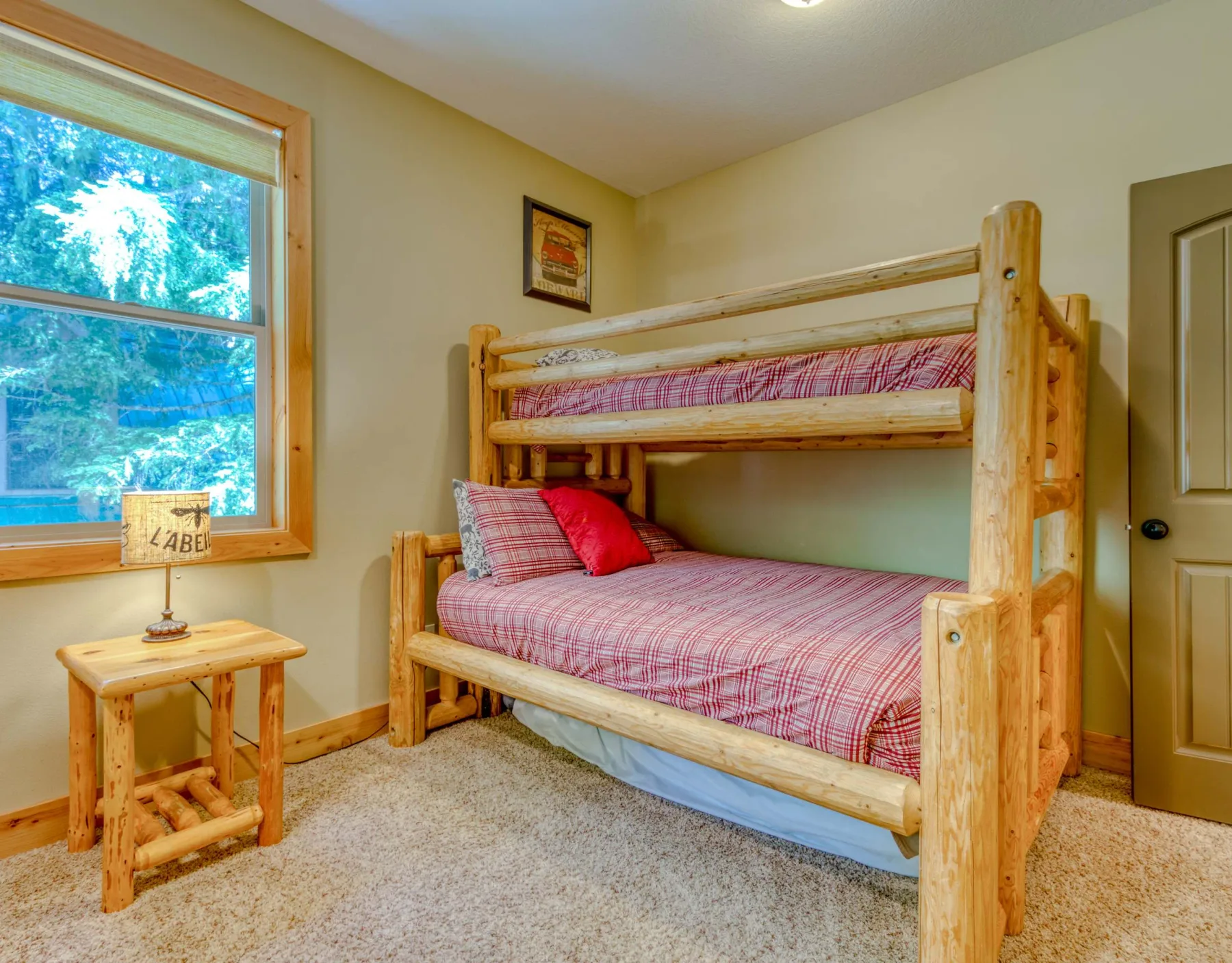 A wooden bunk bed with plaid bedding sits beside a window in a bedroom.