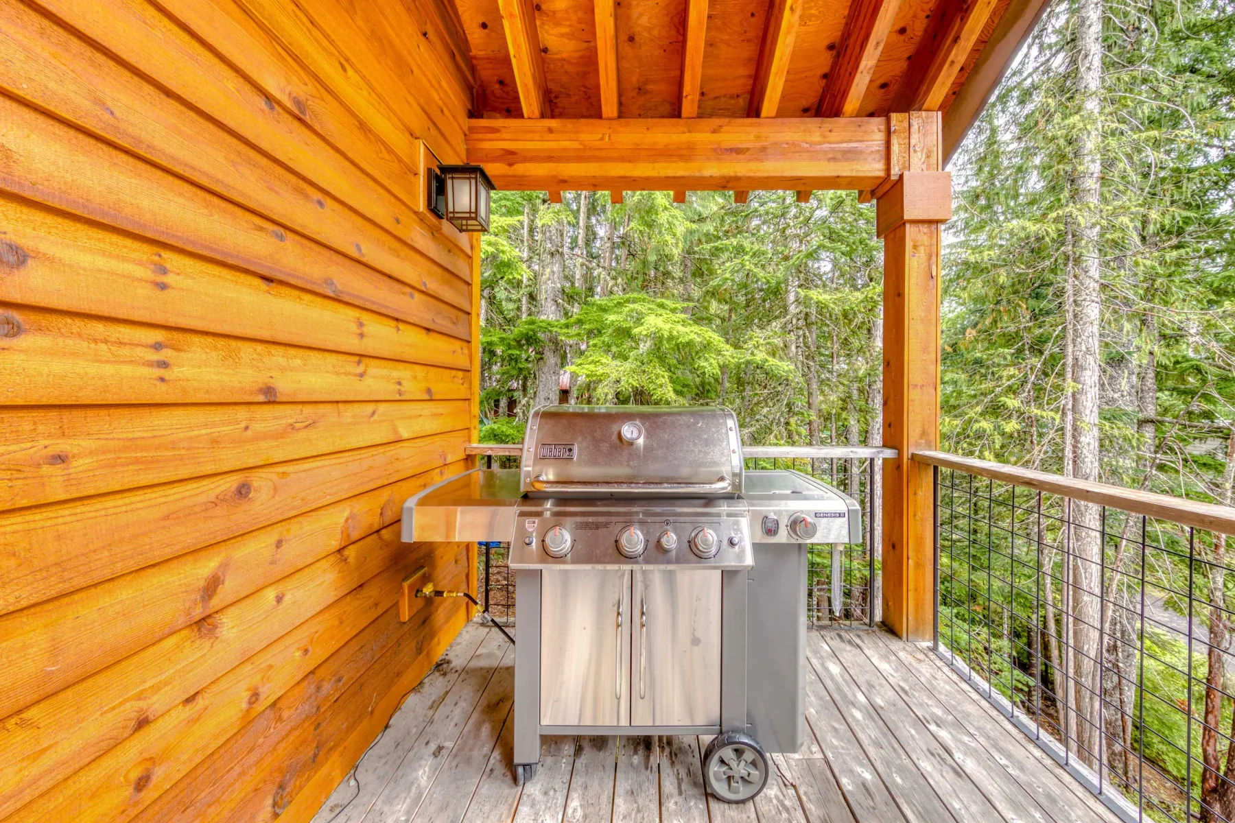 A covered wooden deck with a barbecue grill overlooking trees.