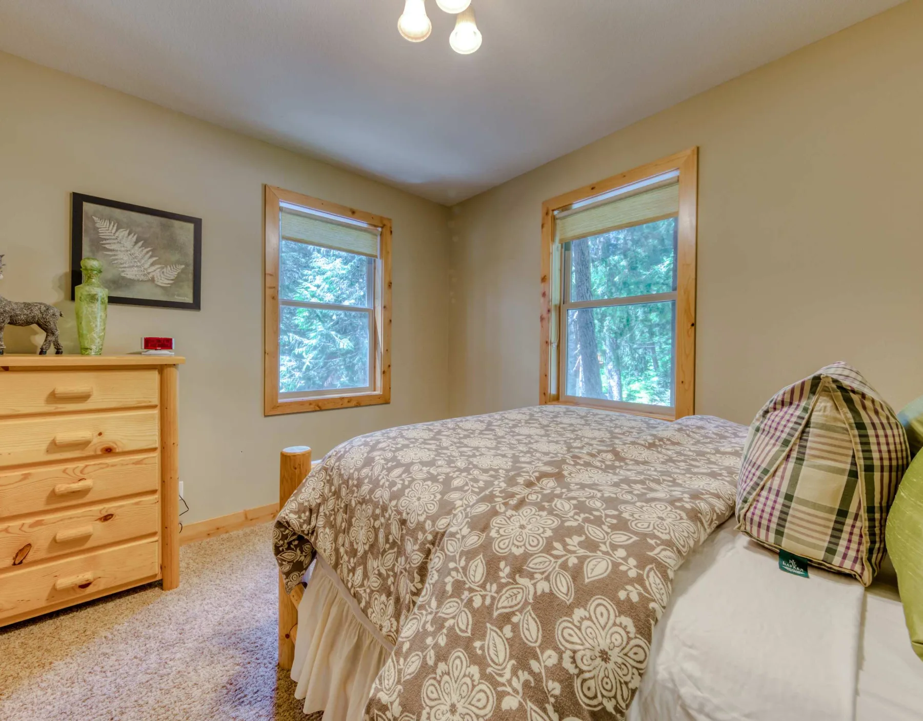A bedroom with a patterned bedspread and two windows overlooking trees.