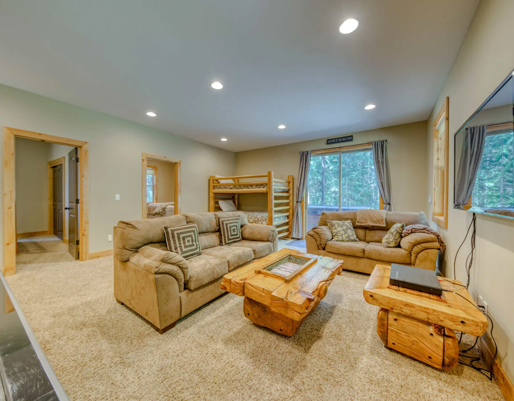 Living room with seating, wooden coffee tables, and a window overlooking trees.