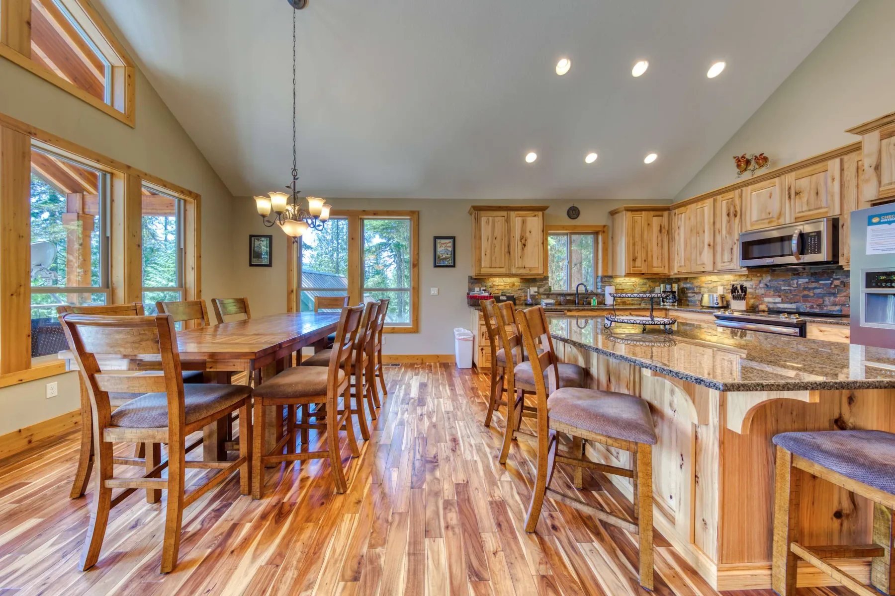 A bright open kitchen and dining area with a long wooden table and breakfast bar.
