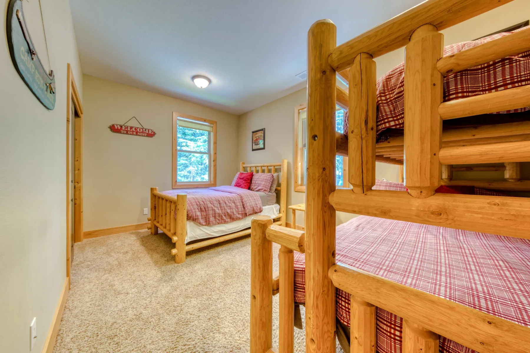 A bedroom with wooden bunk beds and a separate bed beneath two windows.