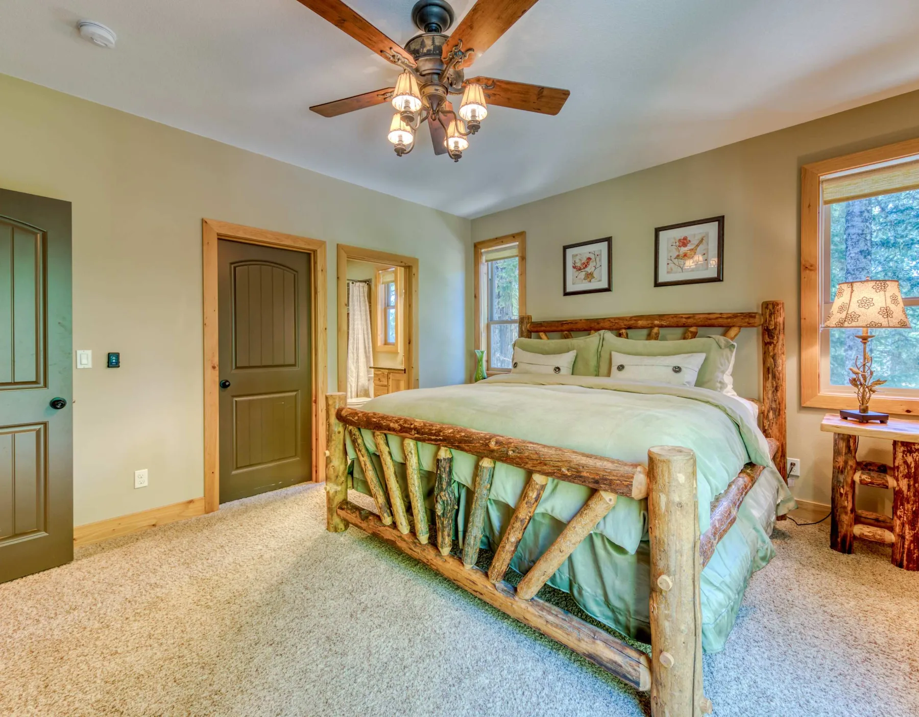 A bedroom with a wooden bed, pale bedding, and windows along the wall.