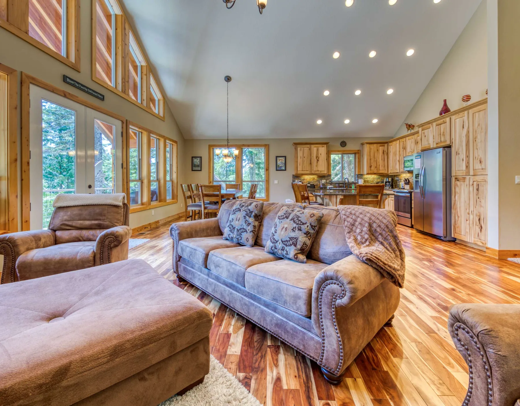 A spacious living room opens into a kitchen, with seating beneath tall windows.