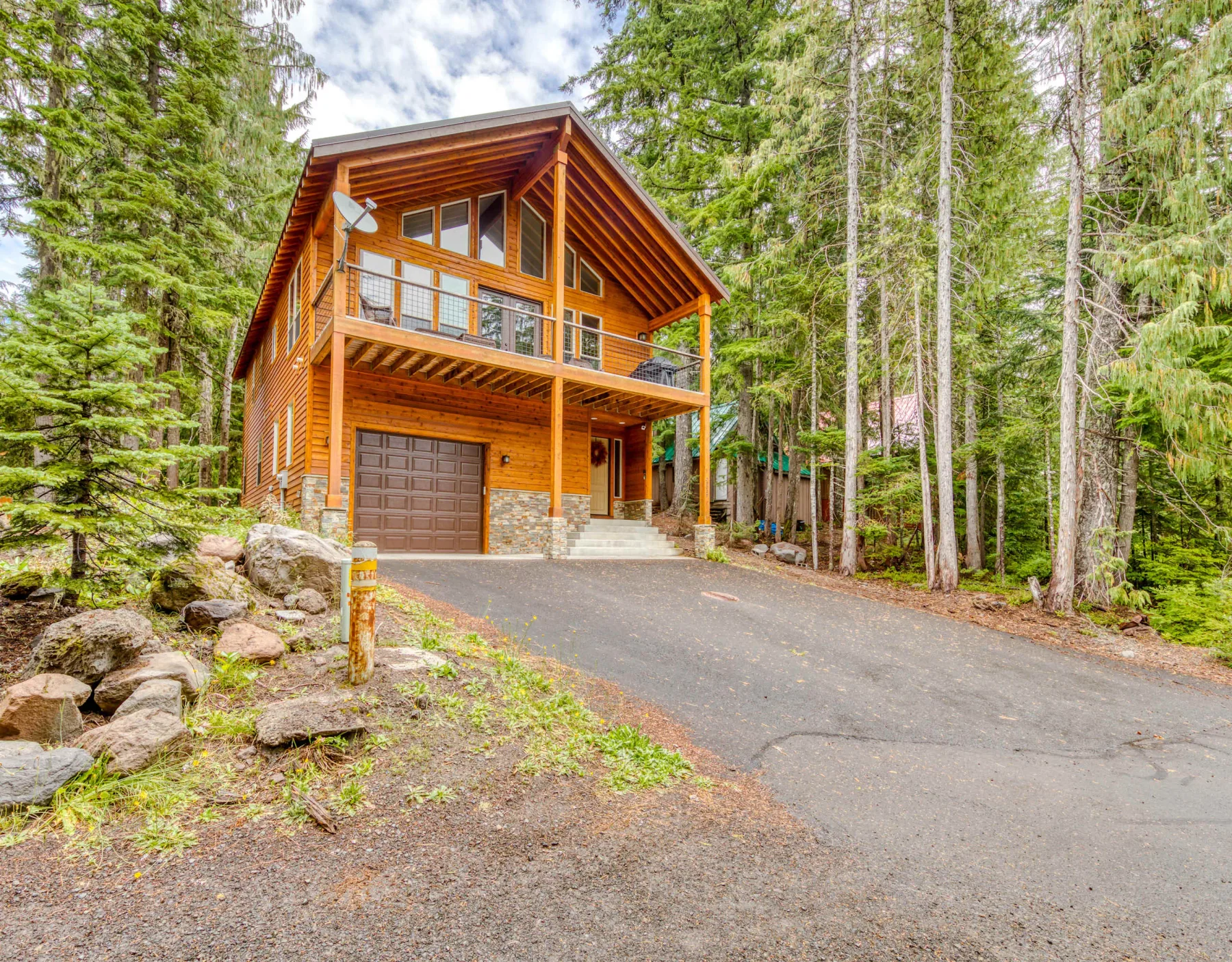 A wooden cabin stands among trees beside a paved driveway.