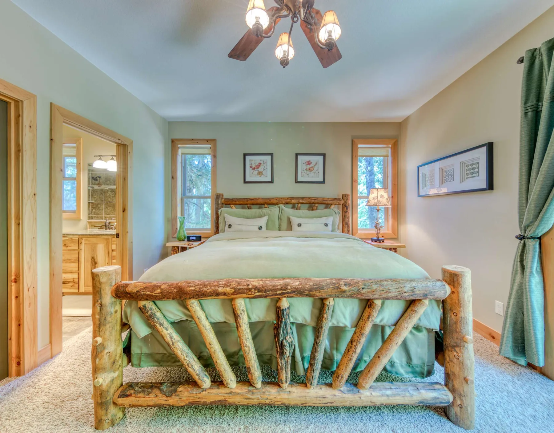 A bedroom with a wooden bed, green bedding, and windows beside the headboard.