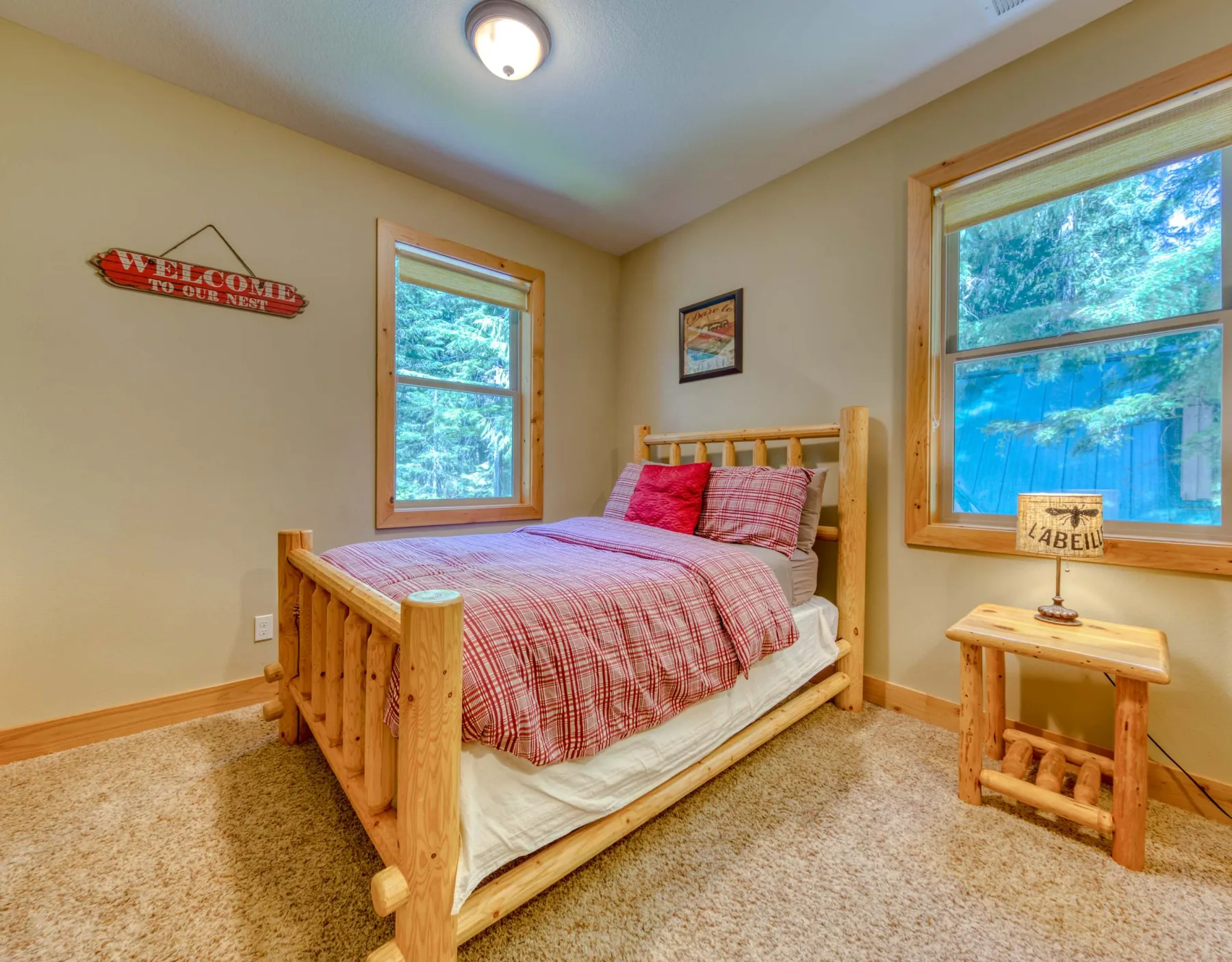 A bedroom with a wooden bed, red plaid bedding, and windows overlooking trees.