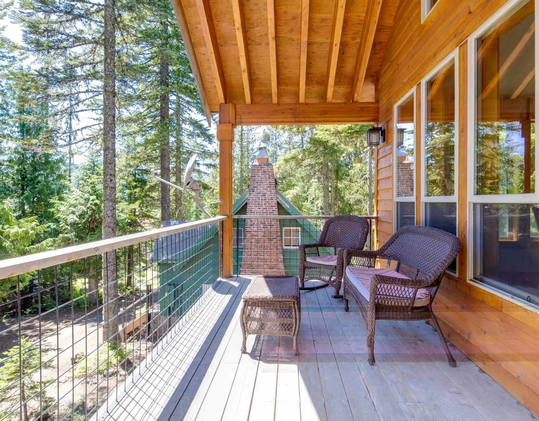A covered wooden deck with outdoor seating overlooks a wooded area.