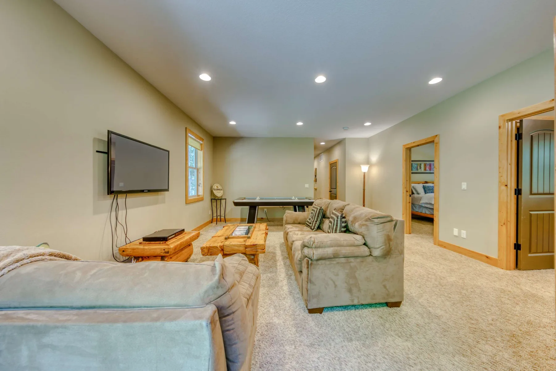 A carpeted living room with seating, a television, and a pool table.