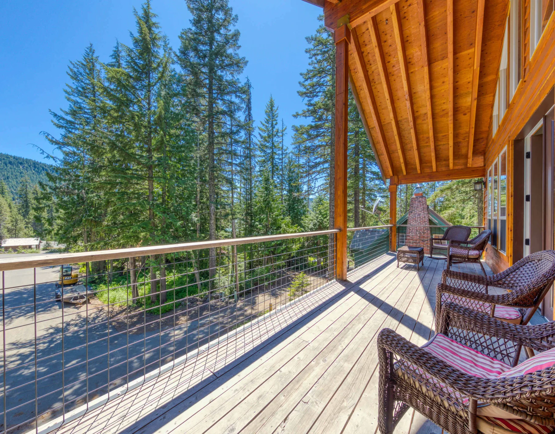 A wooden deck with outdoor seating overlooks tall trees and a road.