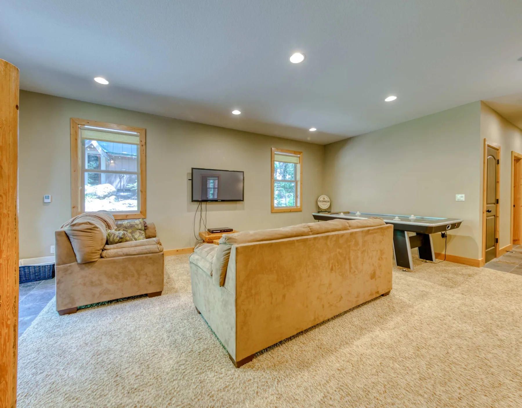A carpeted living room with seating, a wall-mounted television, and a pool table.