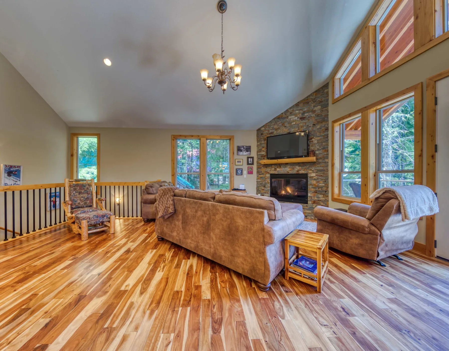 A spacious living room with seating, a stone fireplace, and large windows.