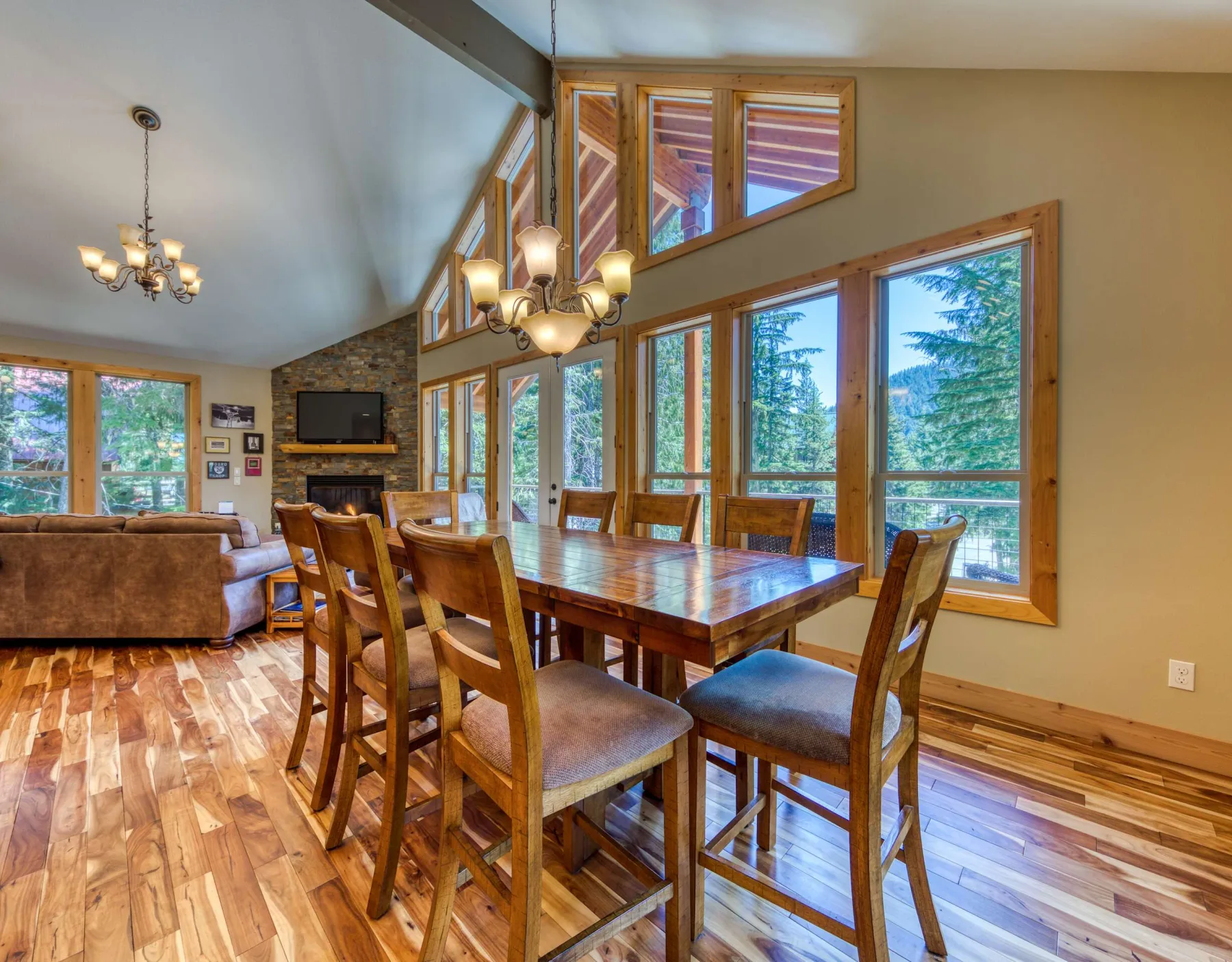 A dining area with a wooden table and chairs beside large windows.
