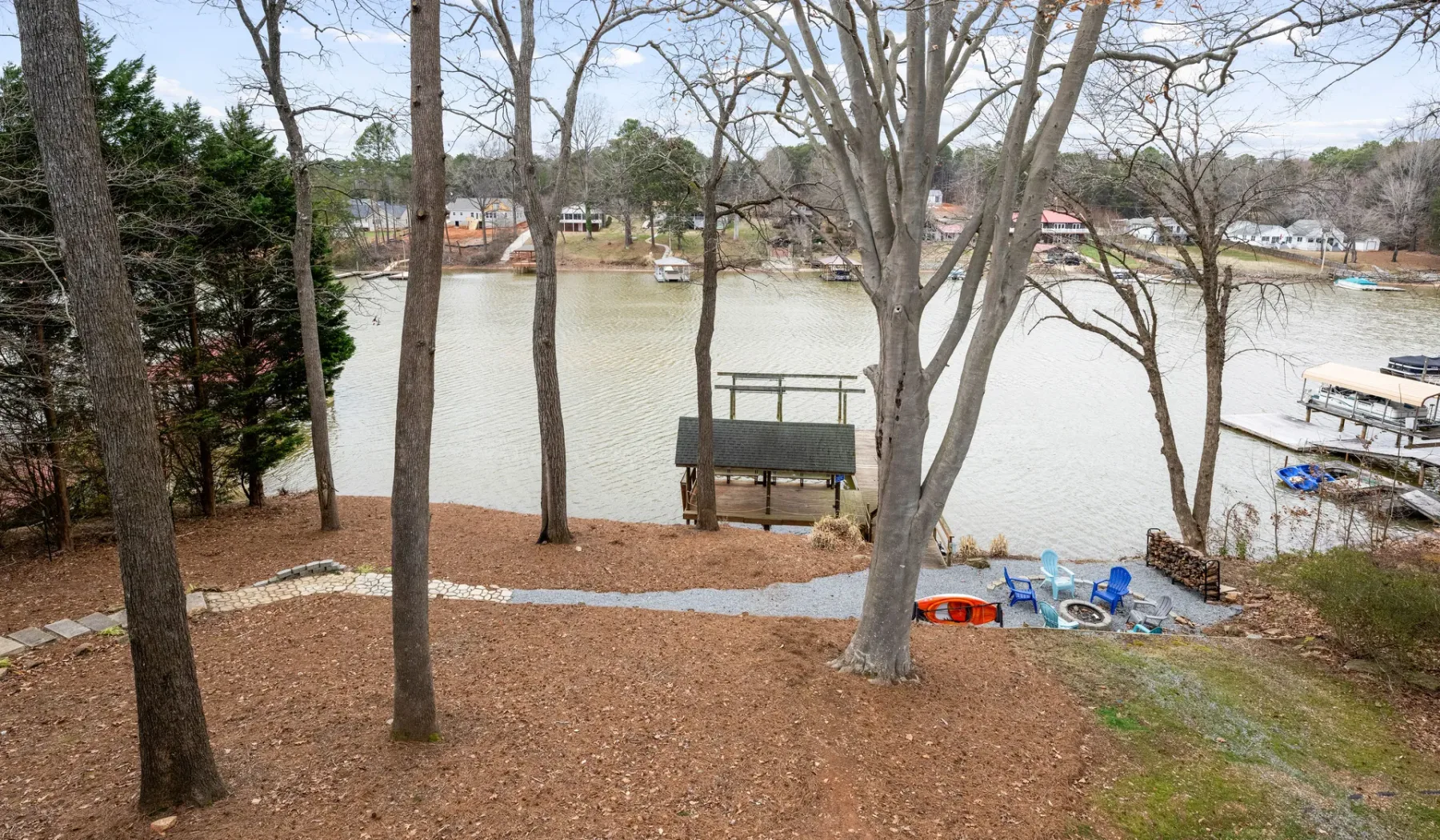 A wooded lakeside view with a small dock and boats on the water.