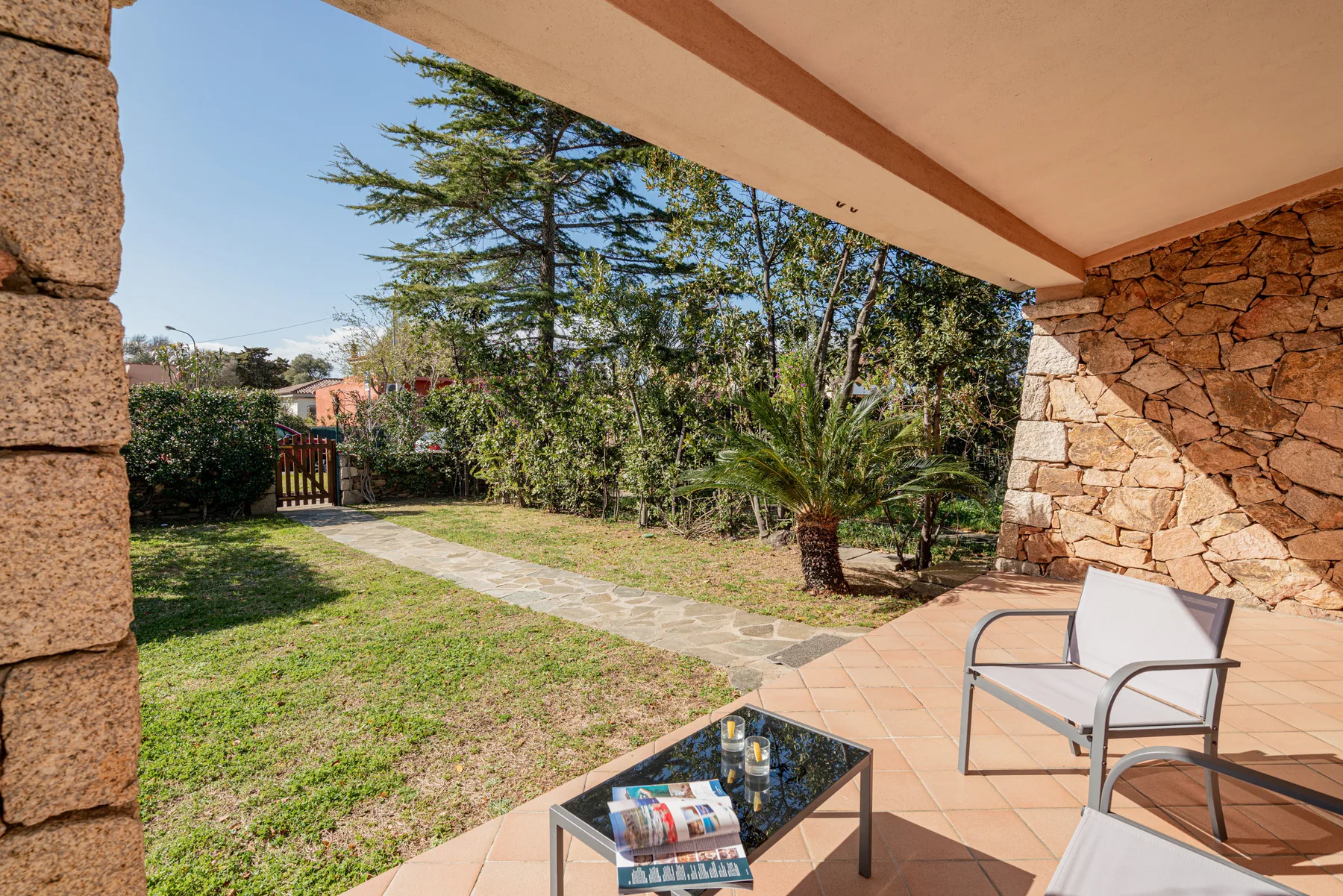 Un patio cubierto con asientos da a un jardín y un sendero de piedra.