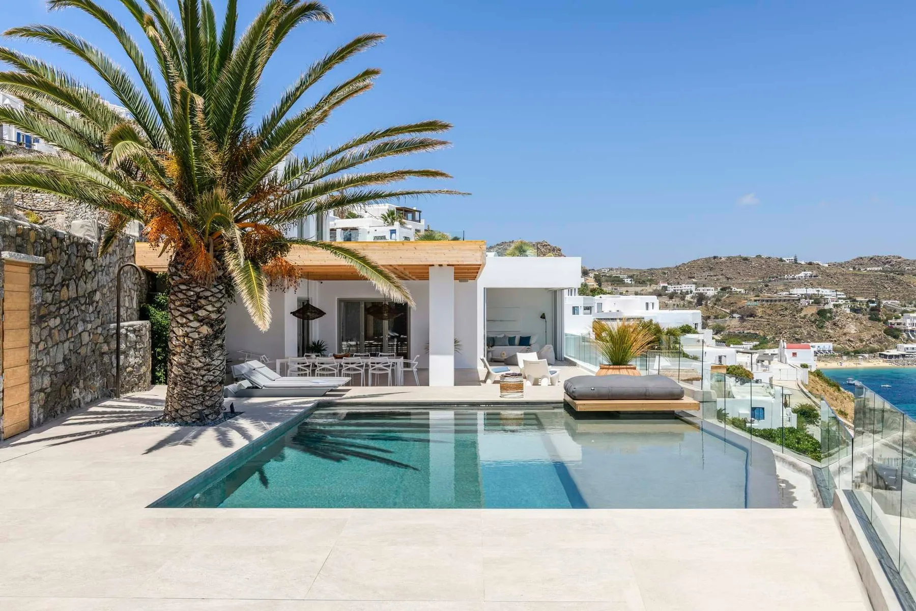 Una terraza soleada con piscina, asientos, una palmera y vistas a las colinas cercanas.