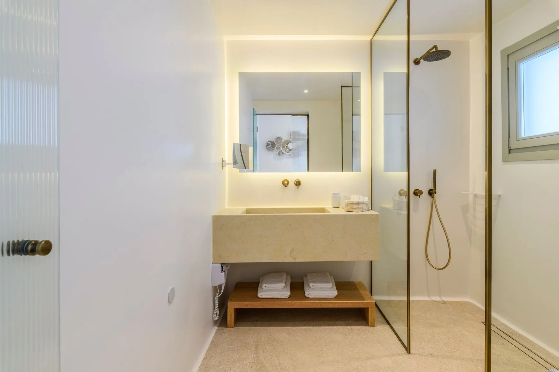 Un baño luminoso tiene un lavabo suspendido y una ducha con mampara de vidrio.