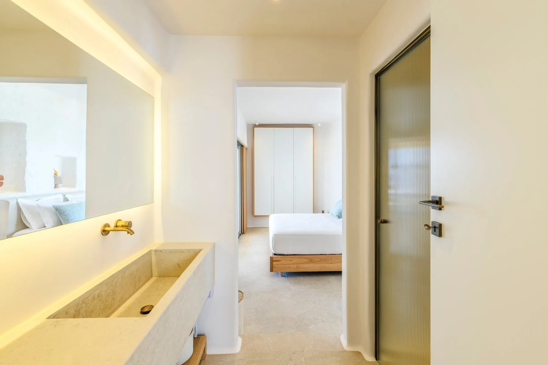 Un tocador de baño luminoso se abre a un dormitorio con una cama.