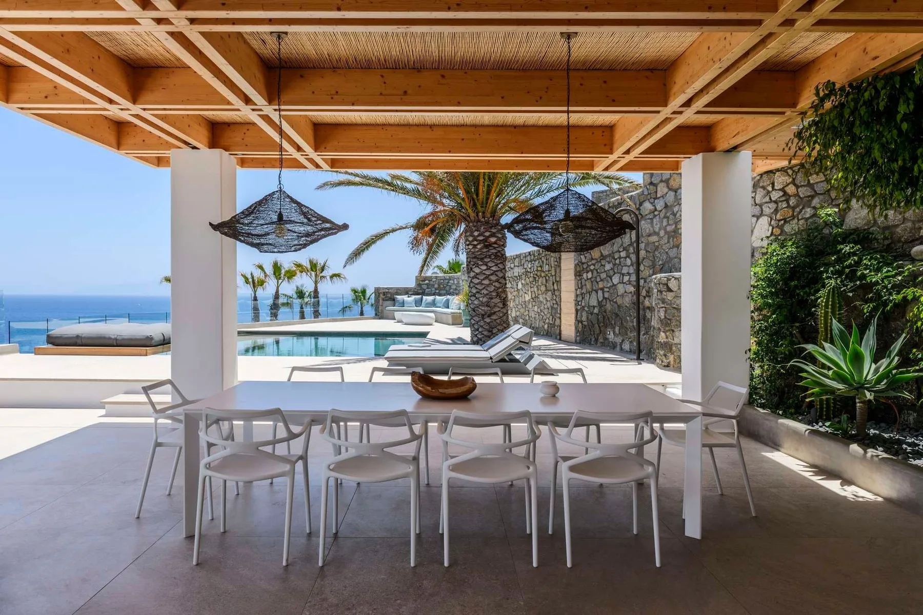 Una zona cubierta de comedor al aire libre da a una piscina y al mar.
