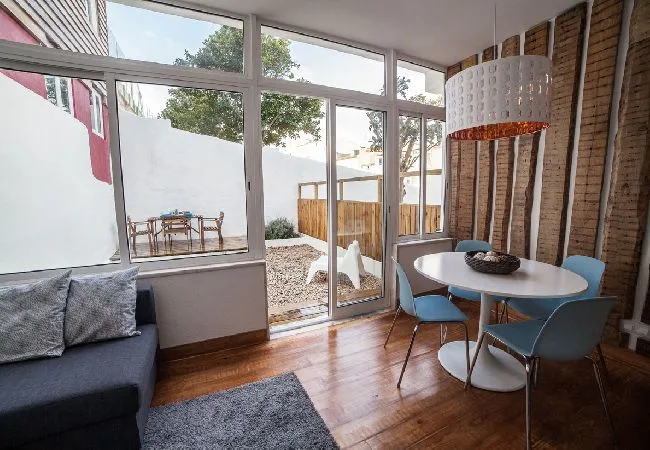 A bright living area with seating, a dining table, and large windows opening to a patio.