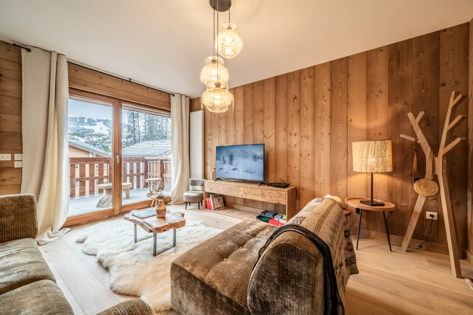A wood-paneled living room with seating, a television, and windows opening onto a balcony.