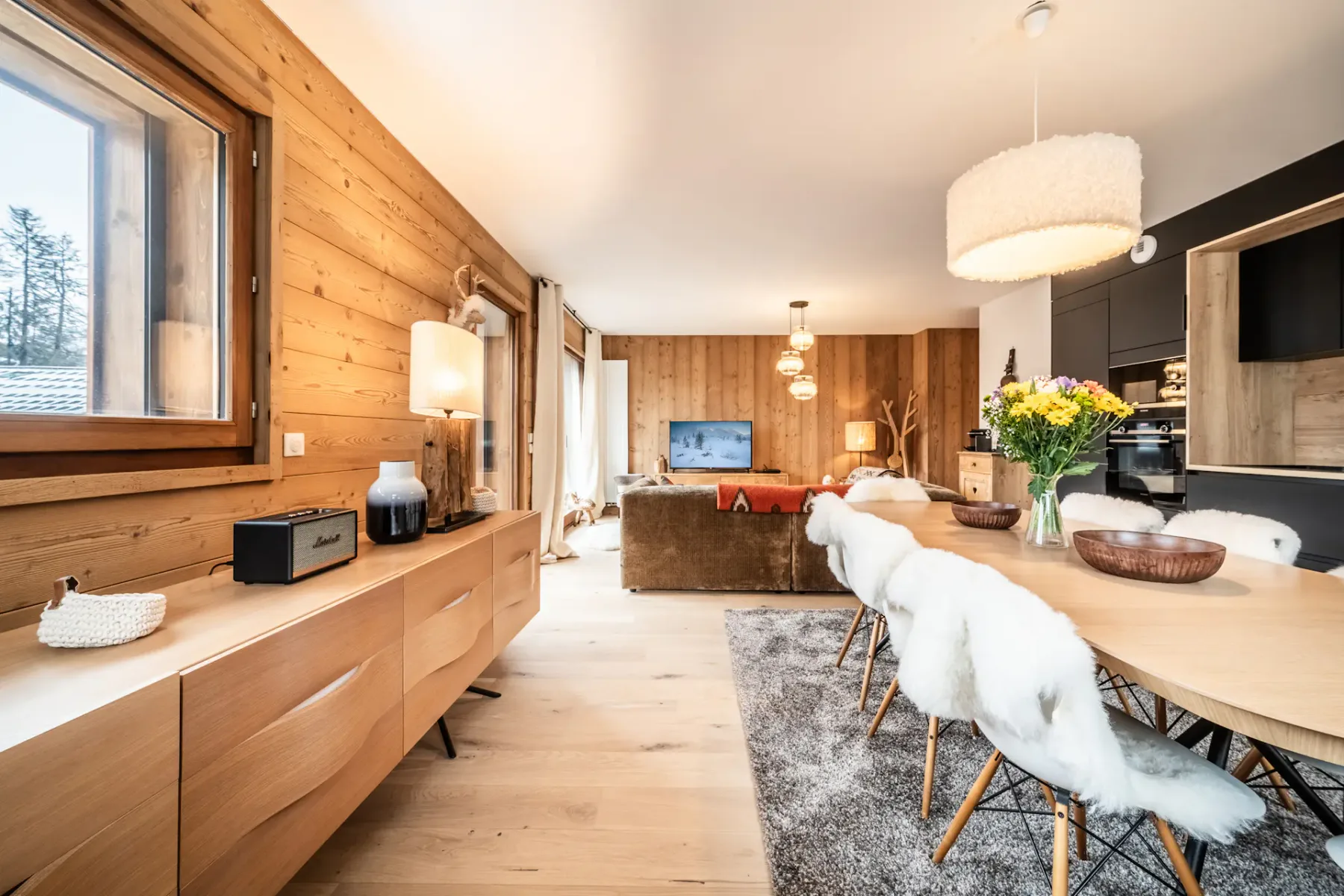 A bright open-plan living and dining area with wood-paneled walls and a long table.
