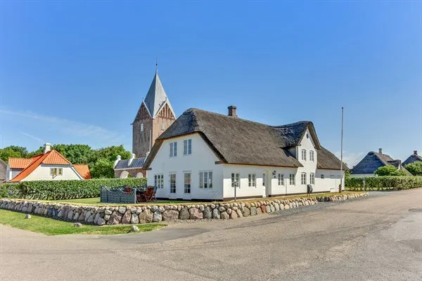 A white building with a steep roof stands beside a quiet road under a blue sky.