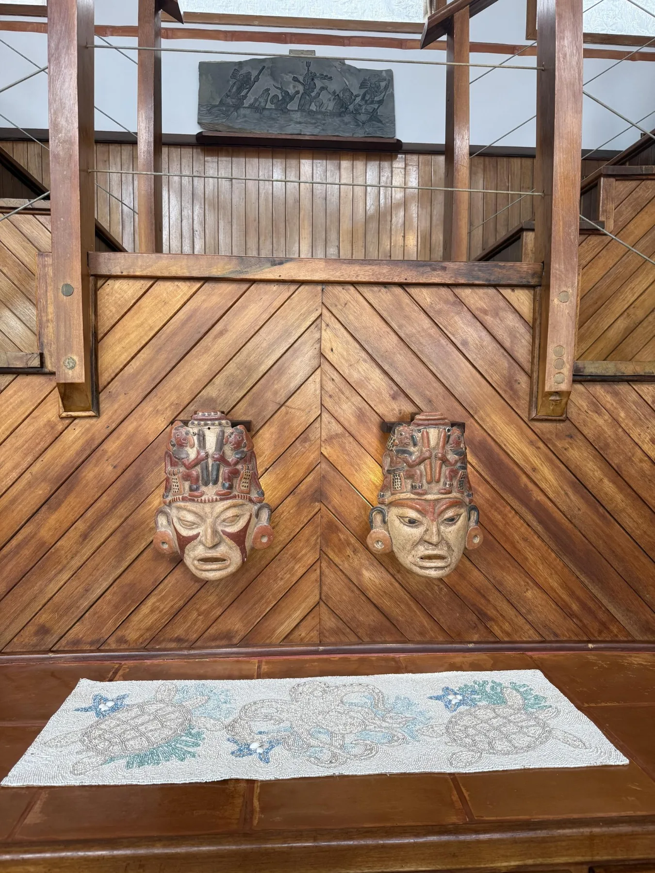 Una pared interior de madera muestra dos máscaras talladas sobre una alfombra estampada.