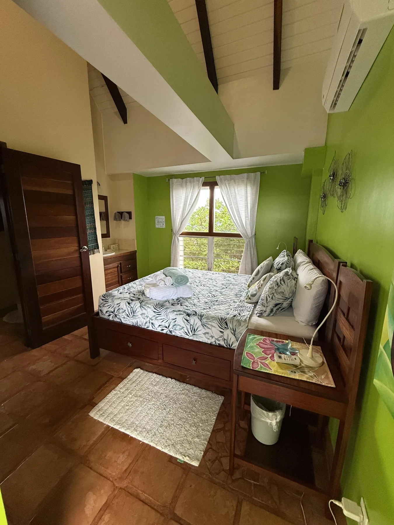 Un dormitorio con una cama de madera, ropa de cama estampada y una ventana con cortinas blancas.