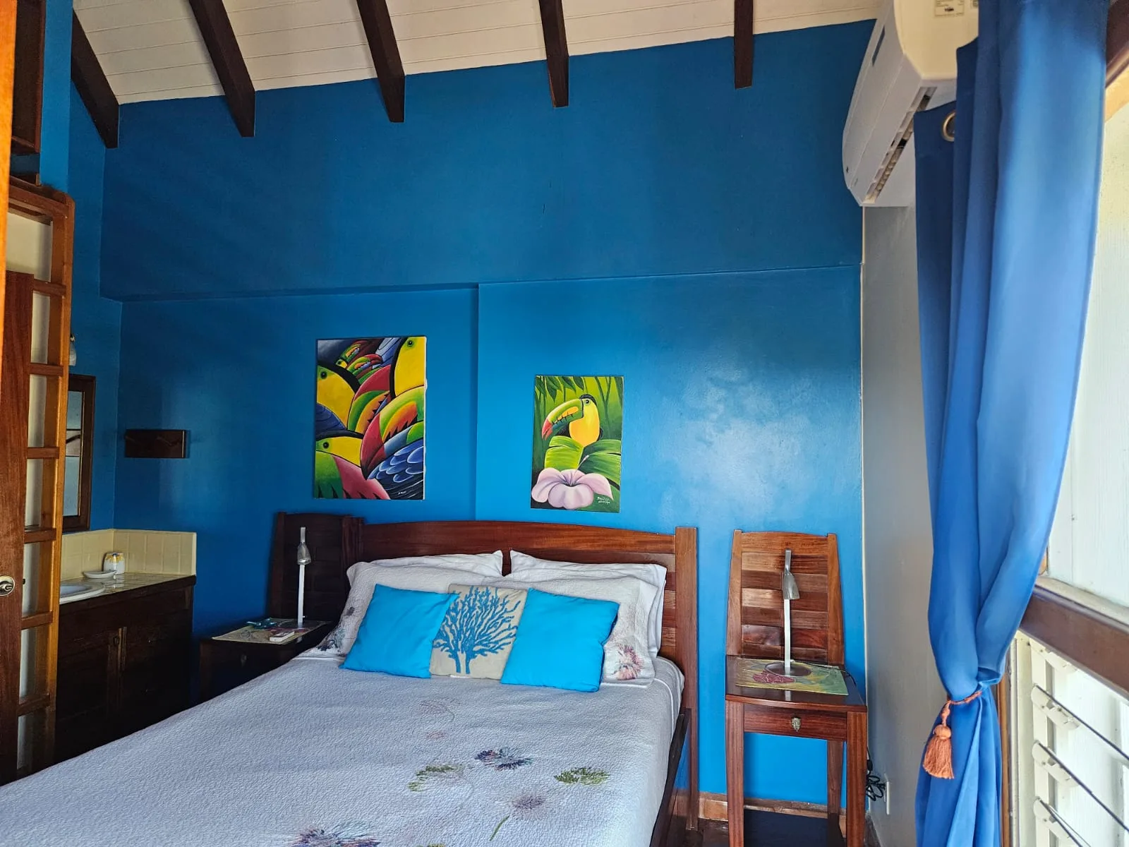 Un dormitorio con una cama junto a paredes azules y cuadros coloridos.