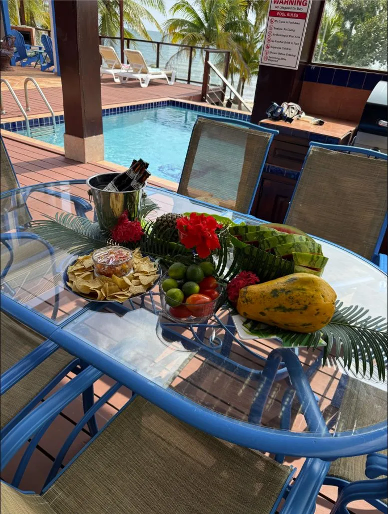 Una mesa de vidrio en el patio exhibe fruta fresca junto a una piscina.