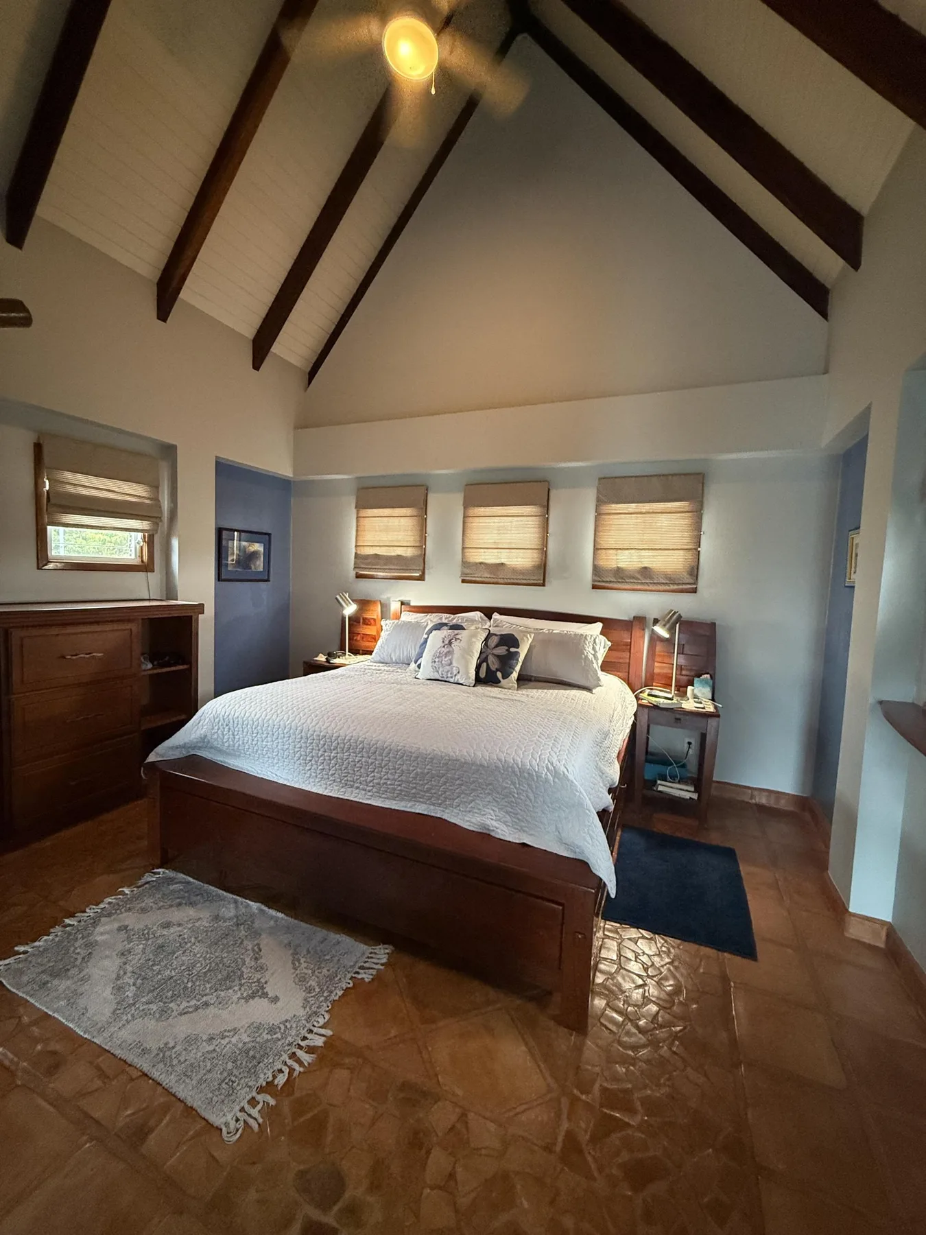 Un dormitorio con una cama bien hecha bajo un techo alto con vigas.