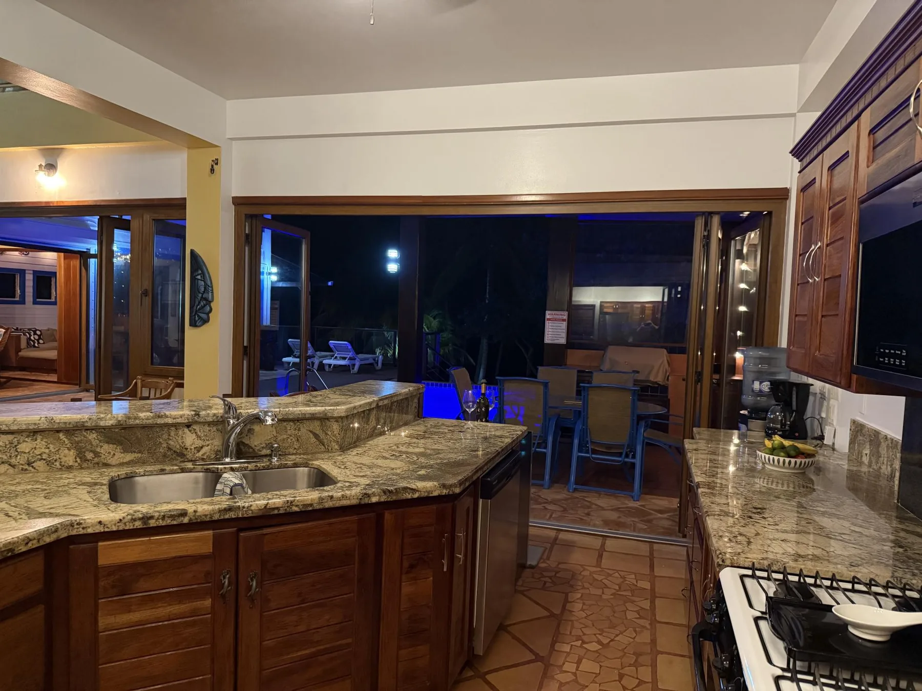 Una cocina con encimera de piedra, gabinetes de madera y una mesa junto a las ventanas.